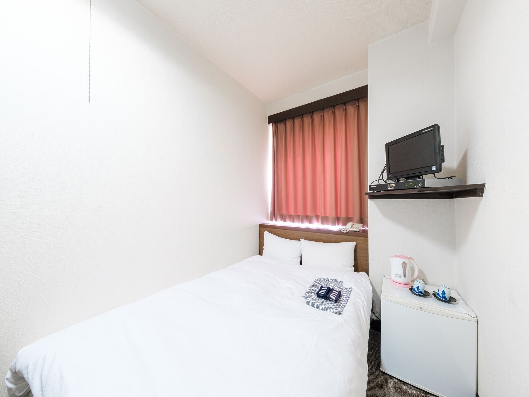 Une chambre d’hôtel équipée d’un lit, d’un téléviseur posé sur une étagère, d’une machine à café et d’un téléphone.