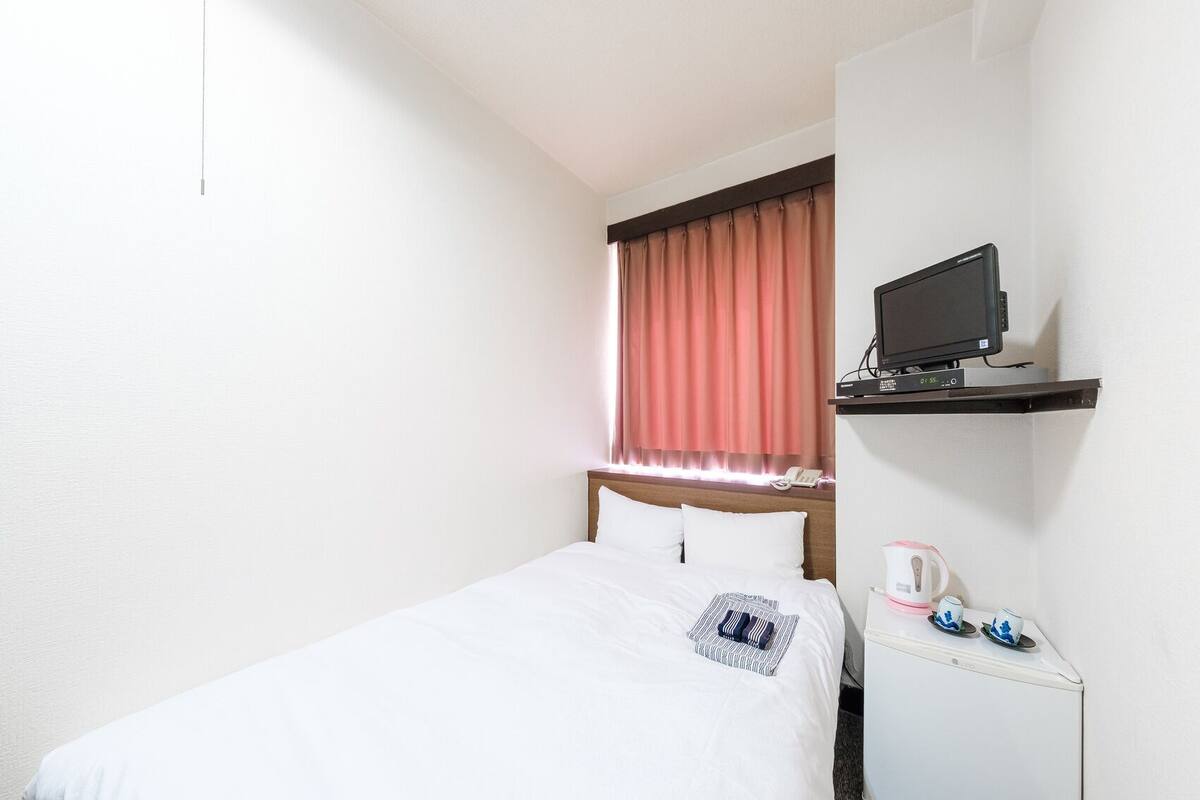 Une chambre d’hôtel équipée d’un lit, d’un téléviseur posé sur une étagère, d’une machine à café et d’un téléphone.