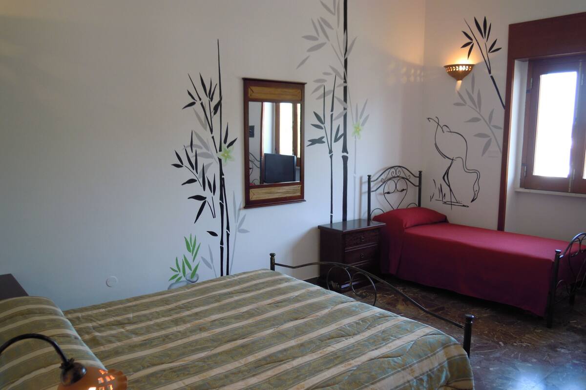 Quarto com cama, mesa de cabeceira, cômoda, cadeira e janela.