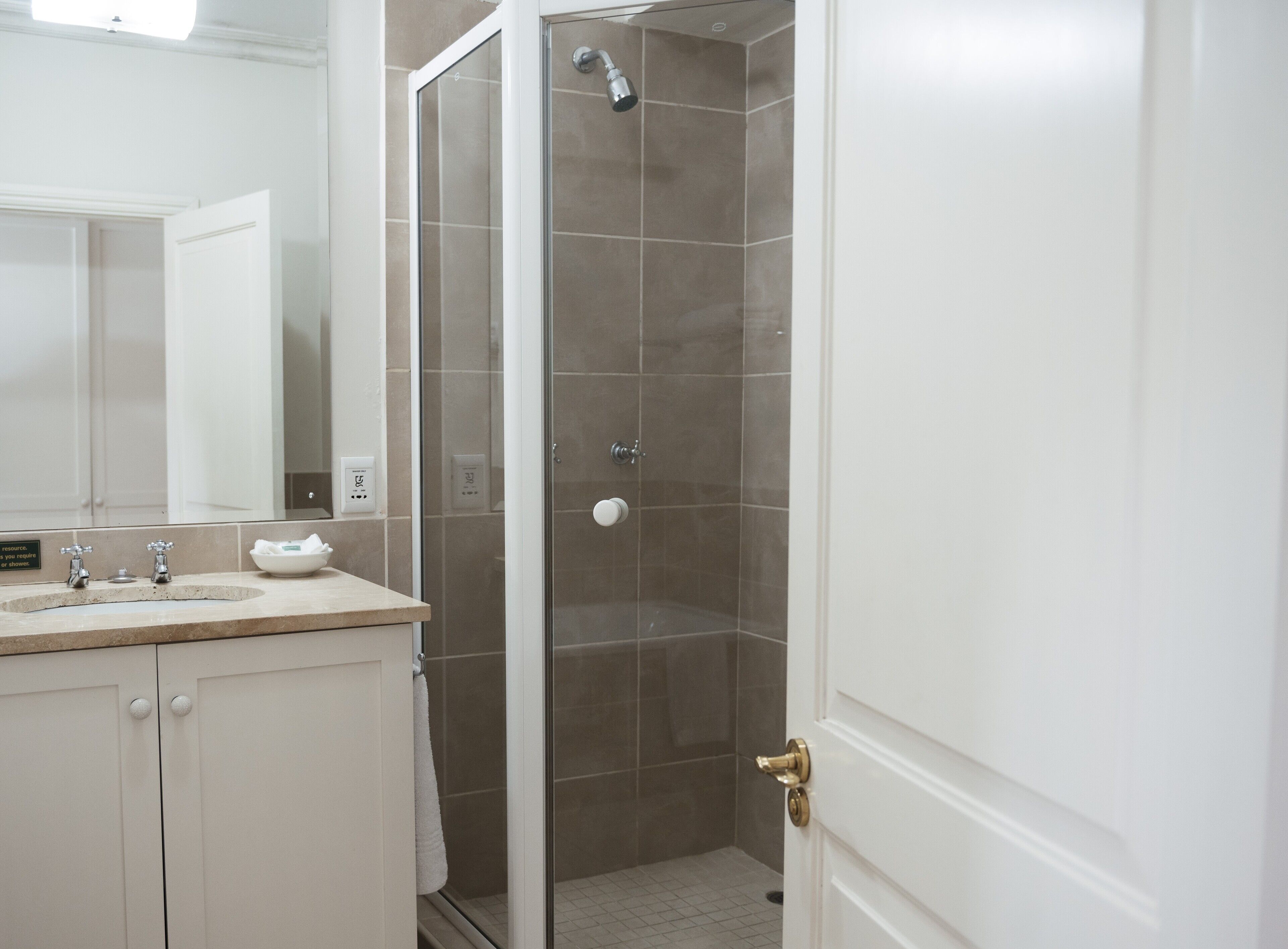 Une salle de bain avec une douche à parois de verre, un lavabo avec deux robinets et un miroir.