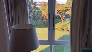 A room with a view of a well-maintained lawn and trees, a lamp, and a window with curtains. - Redlands Hotel (Pietermaritzburg)