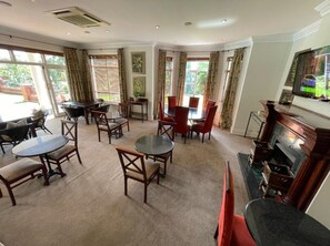 A spacious living room with a fireplace, multiple seating areas, and large windows offering a view of the outdoors. - Redlands Hotel (Pietermaritzburg)