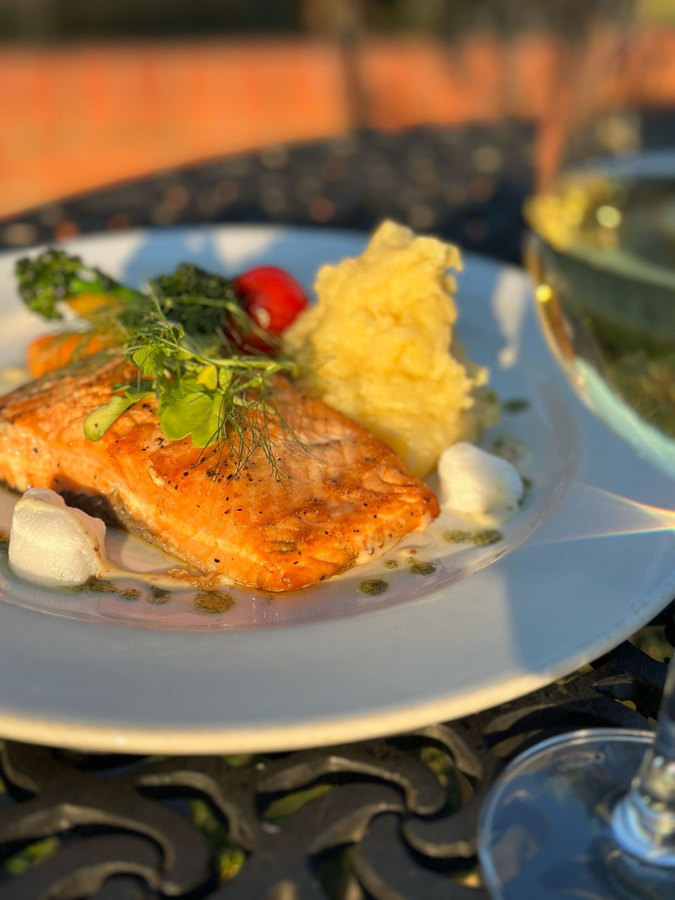 Une assiette contenant un filet de saumon, de la purée de pommes de terre et une petite salade, posée sur une table.