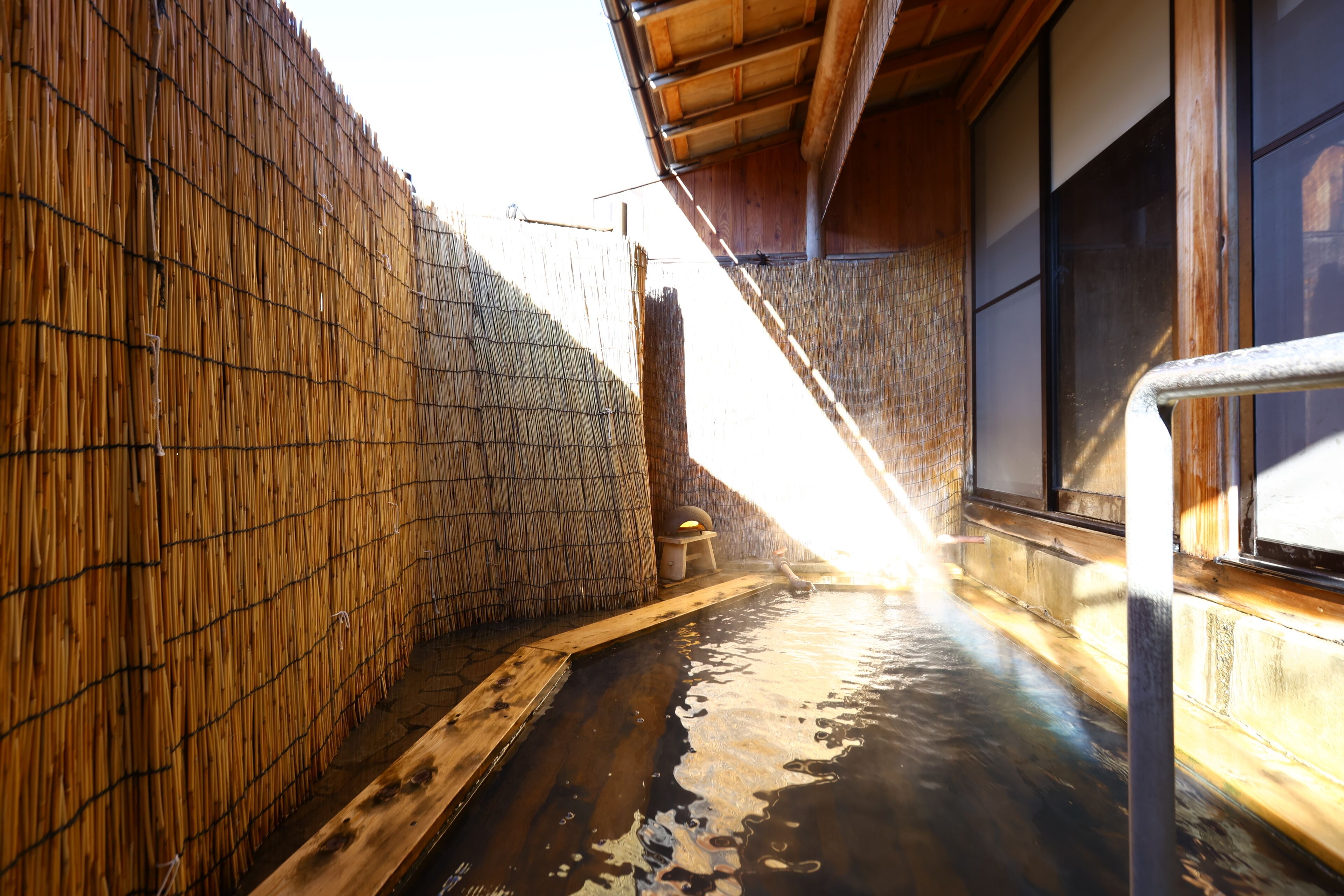 A traditional Japanese onsen with wooden walls and a wooden deck leading into the hot spring.