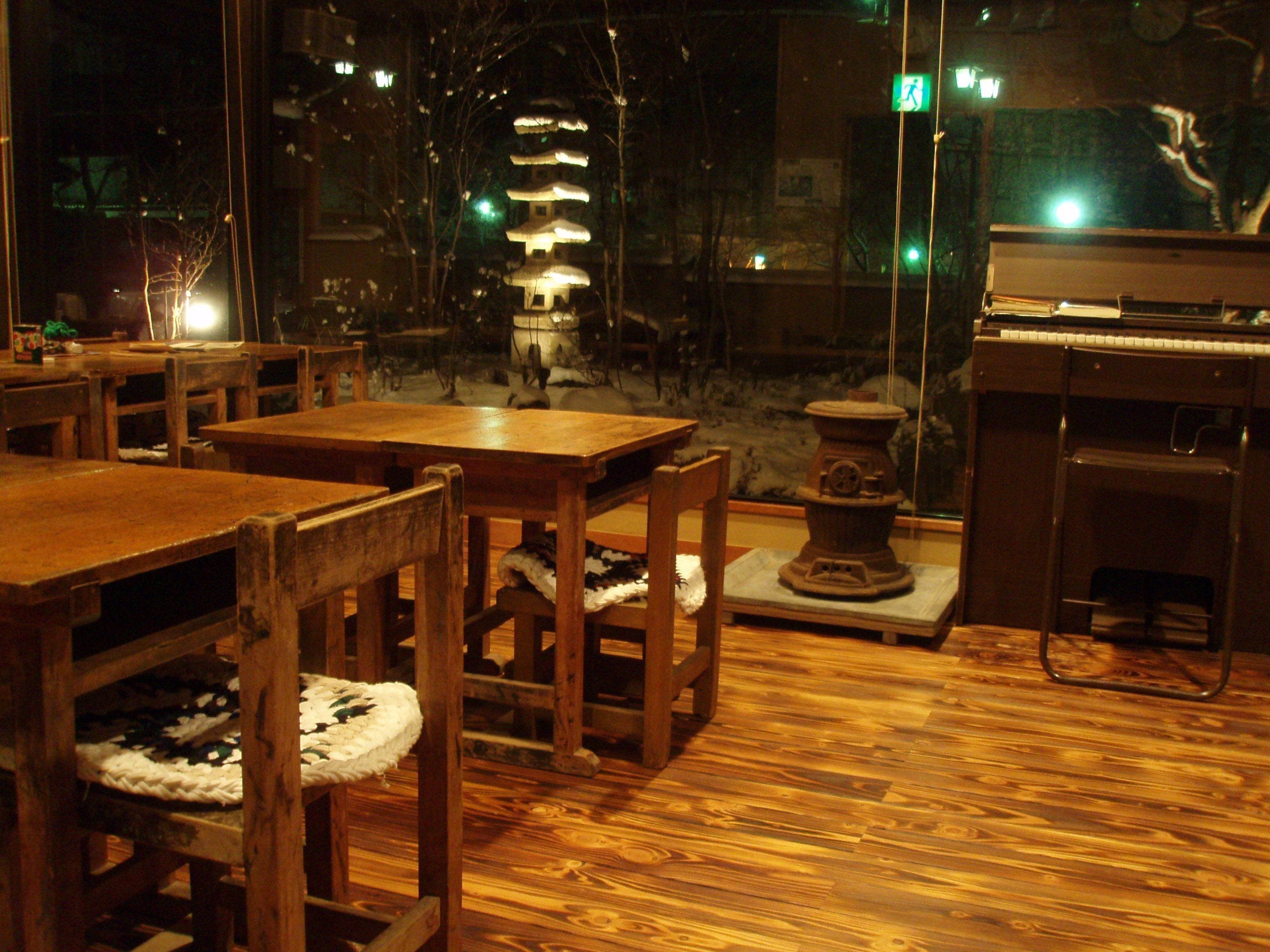 A wooden interior with tables and chairs, a piano, and a traditional Japanese water feature.