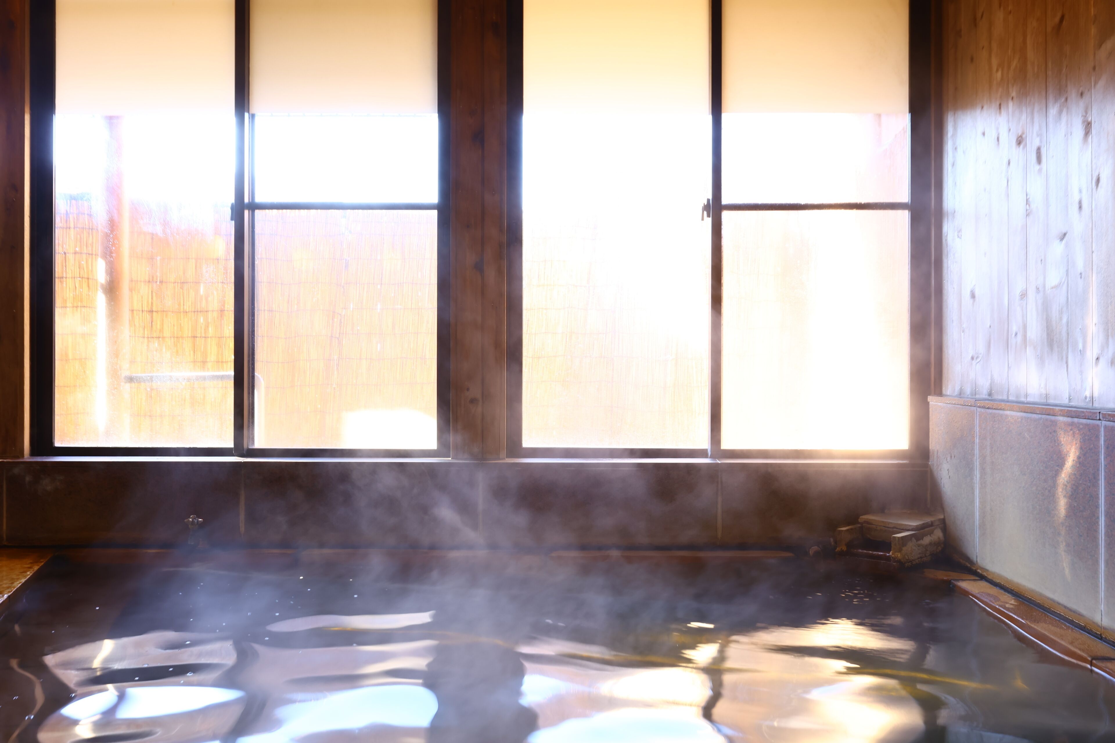 Ein traditionelles japanisches Onsen mit Holzinnenraum, einem Thermalbad und Blick durch einen Shoji-Schirm.