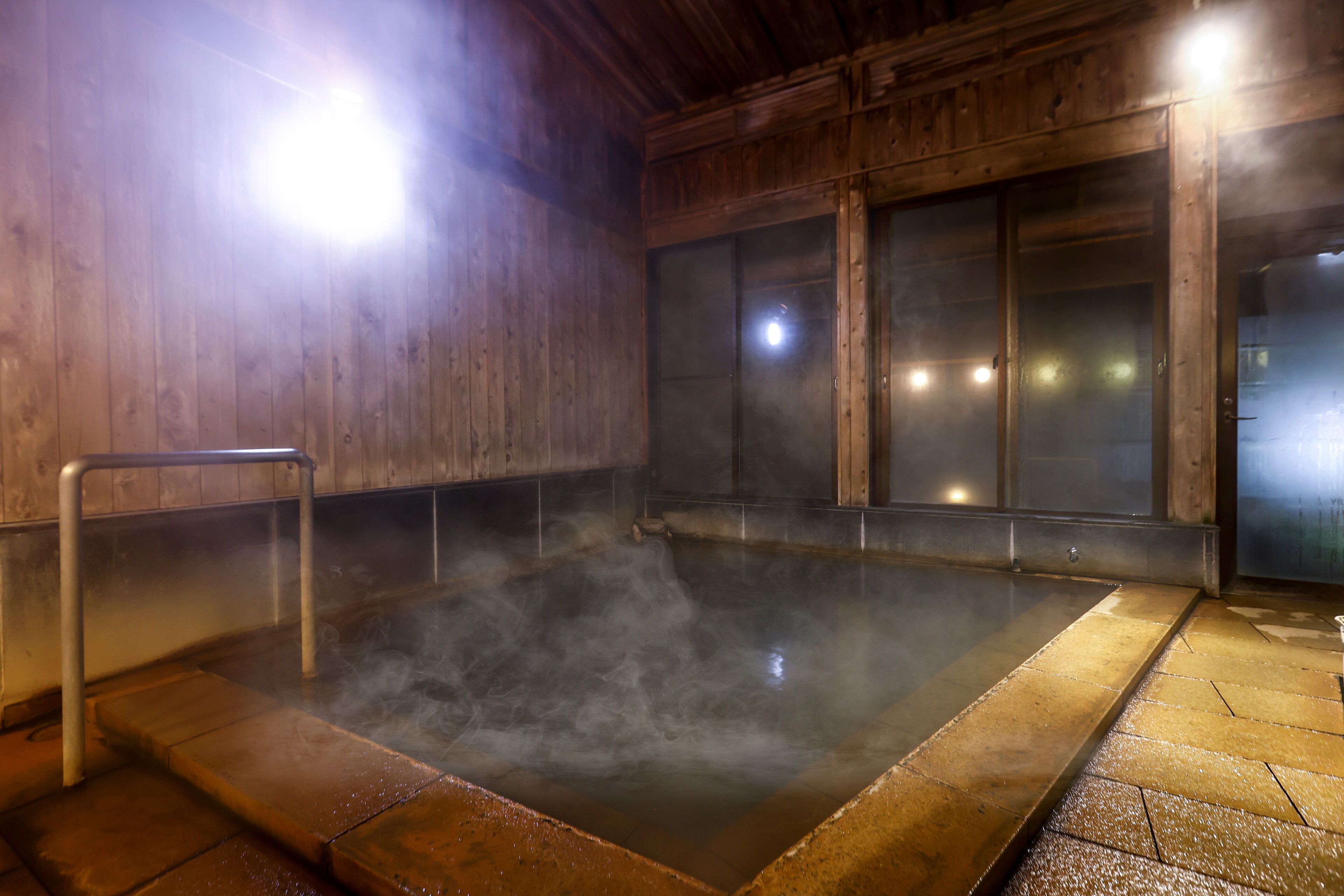A hot spring bath area with wooden walls, a metal railing, and a tiled floor.