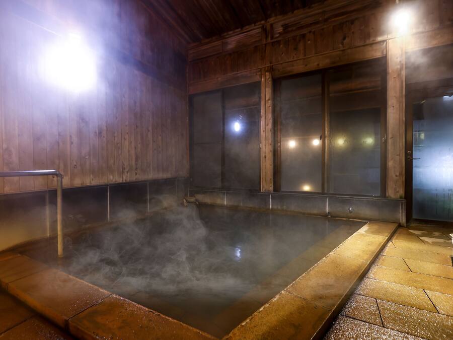 A hot spring bath area with wooden walls, a metal railing, and a tiled floor.