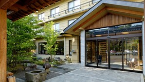 A modern building with a stone-paved courtyard, wooden pergola, and large glass entrance doors. - Shibu Hotel (Yamanouchi)