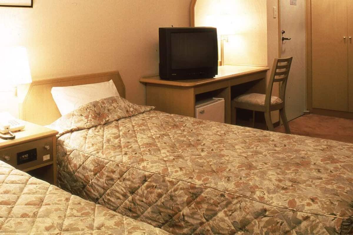 A hotel room with two beds, a desk with a television, a chair, and a wardrobe.
