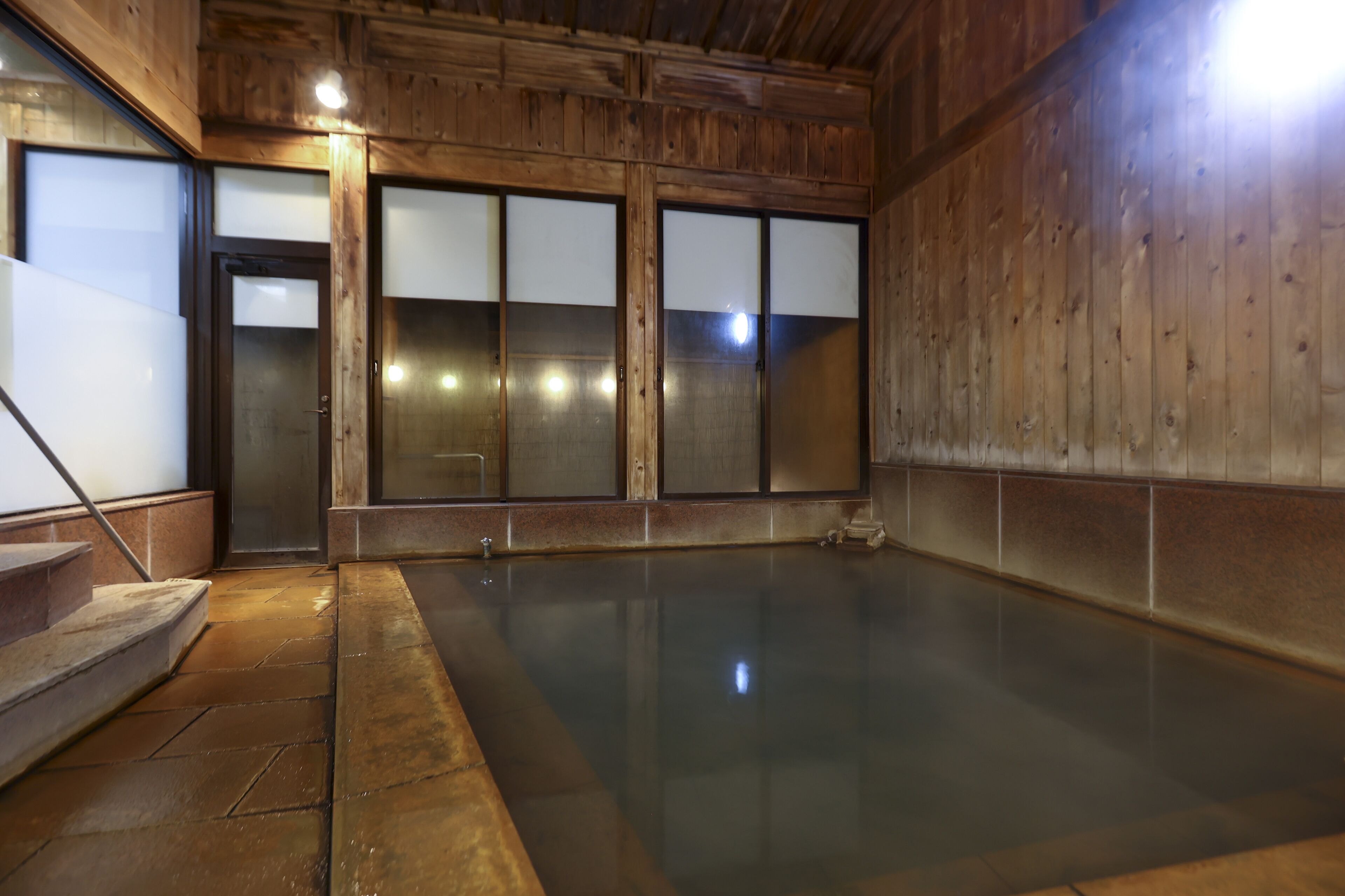 A wooden interior with a large, reflective floor, a set of stairs, and frosted glass doors.