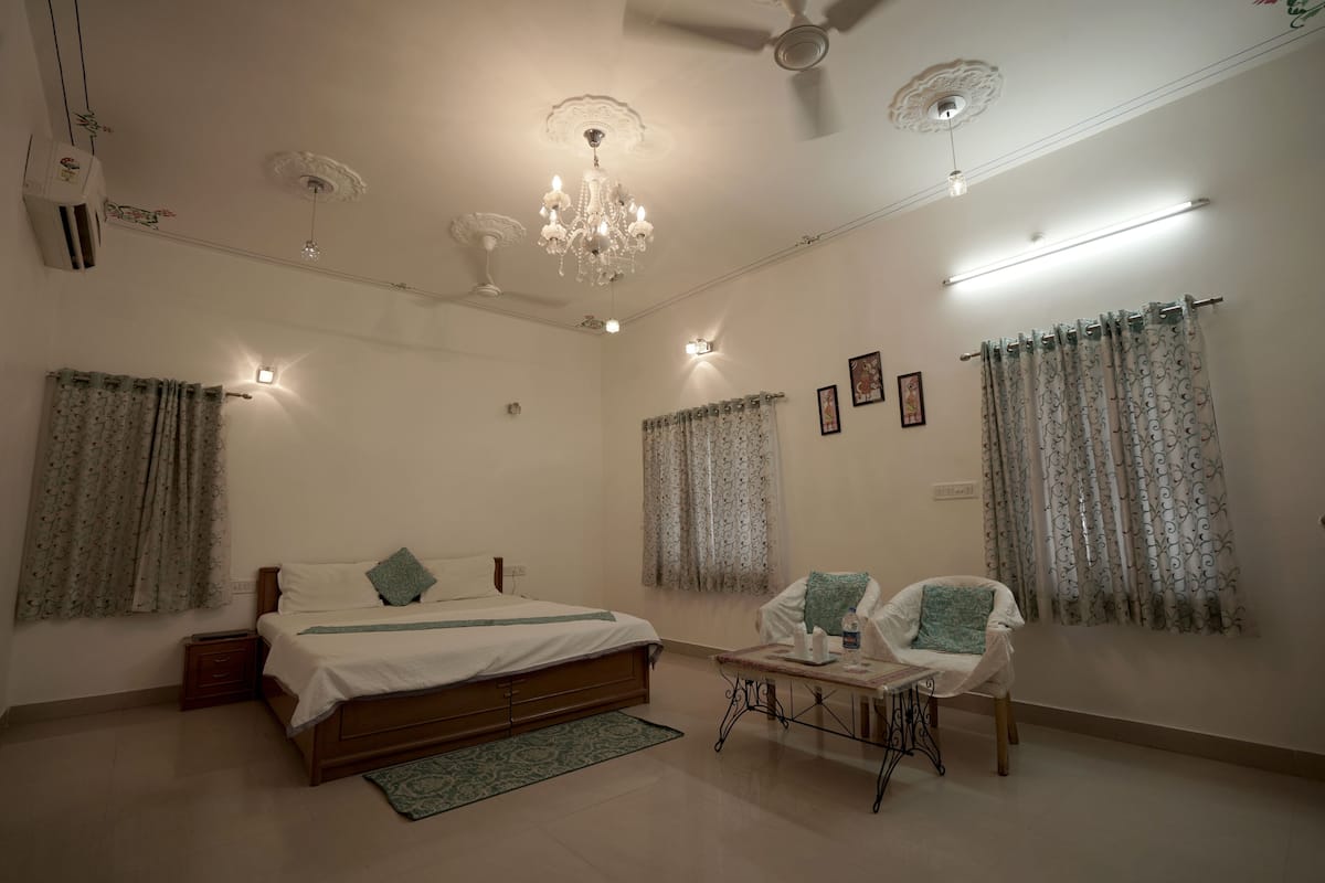 A bedroom with a bed, a chair, a table, and a ceiling fan.