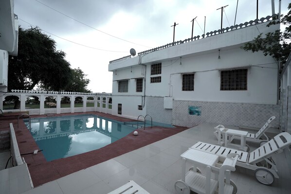 A swimming pool with a red border, white lounge chairs, and a white building with multiple windows and a satellite dish.