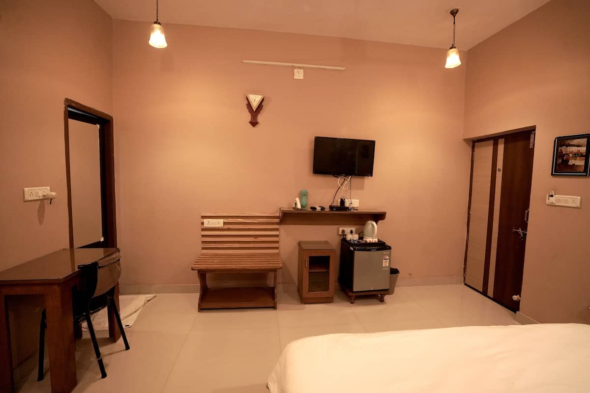 A bedroom with a bed, a desk, a chair, a bench, a TV, a small cabinet, and a wardrobe.
