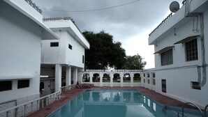 En swimmingpool med en hvid bygning til den ene side og et træ i baggrunden.
