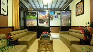 A hotel lobby with a sofa set, a glass coffee table, and a wall with framed pictures.