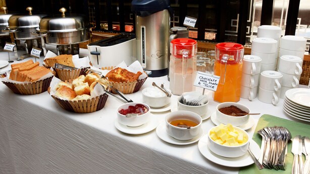 A buffet with various food items and beverages, including a coffee maker, hot water, and a chocolate milkshake.