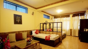 A hotel room with a sofa, two single beds, a dining table with chairs, and a small table with a vase of flowers.