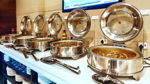 A buffet setup with multiple stainless steel chafing dishes, serving utensils, and a television displaying sports scores.