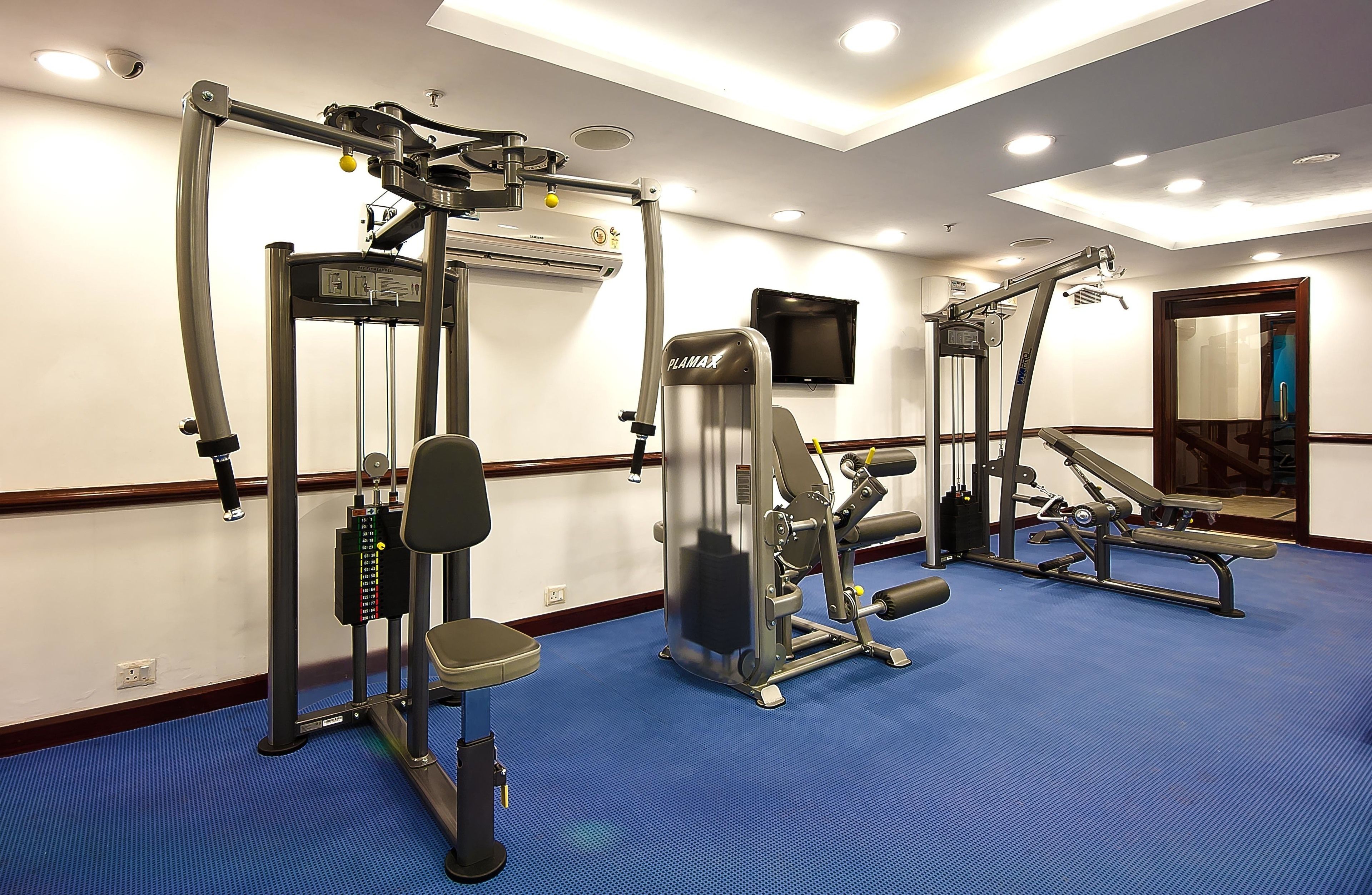 Un gimnasio con diferentes máquinas de ejercicio, un televisor en la pared y un espejo.