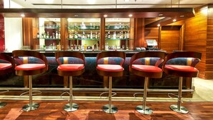 A bar area with four red bar stools and a bar counter stocked with various bottles and glasses.