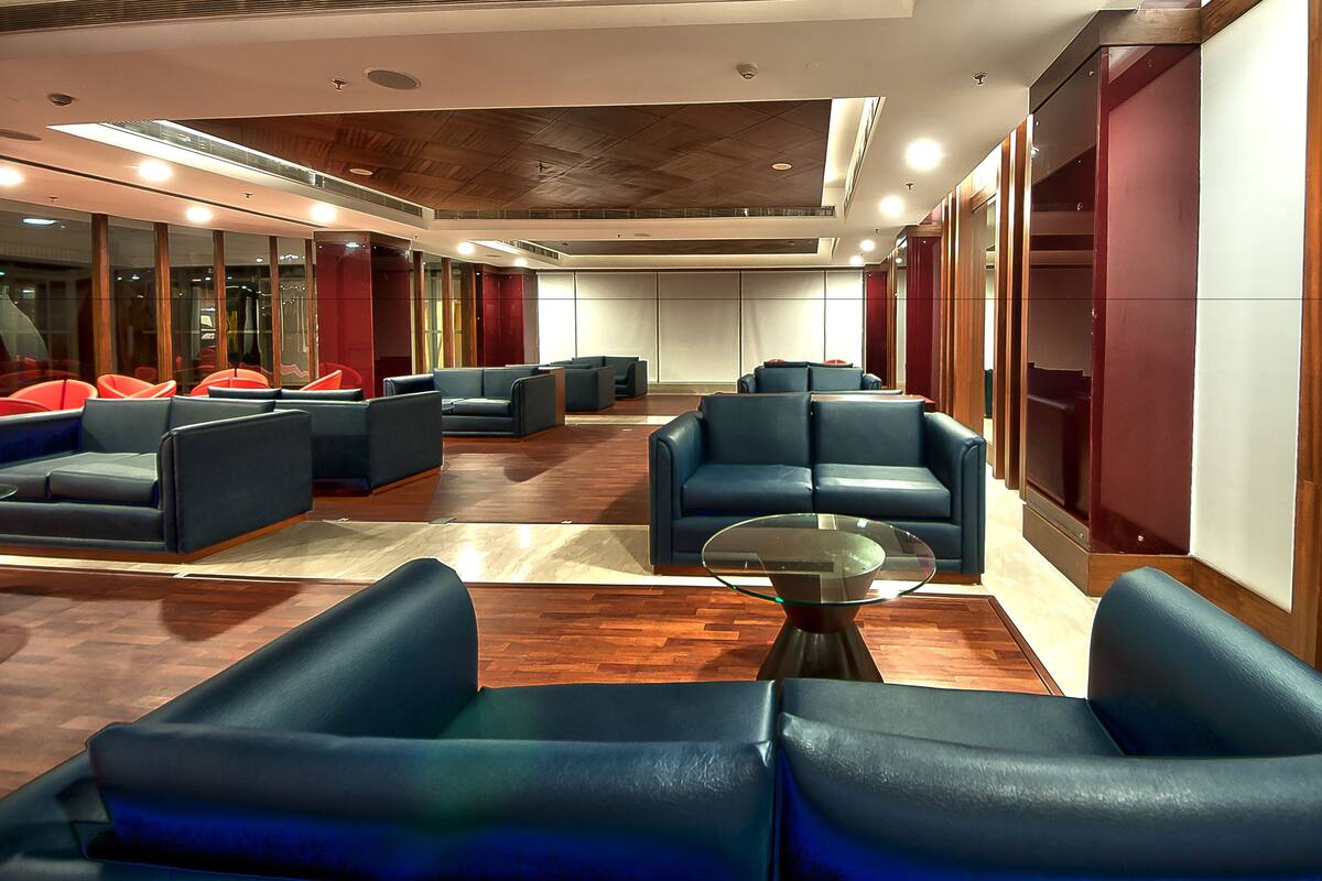 Un hall d’hôtel doté de plusieurs espaces aménagés avec différents types de sièges, notamment des canapés et des fauteuils, disposés autour d’une table basse centrale en verre.