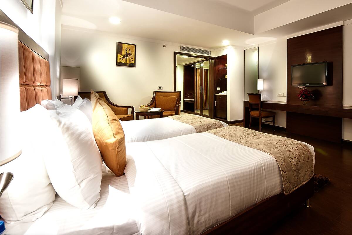 Une chambre d’hôtel avec deux lits, un bureau, une chaise, une télévision et un miroir.