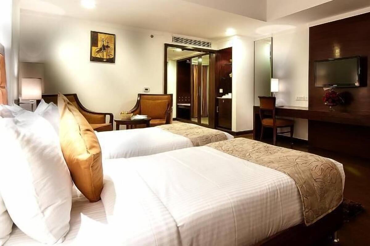 Une chambre d’hôtel avec deux lits, un bureau, une chaise, une télévision et un tableau au mur.