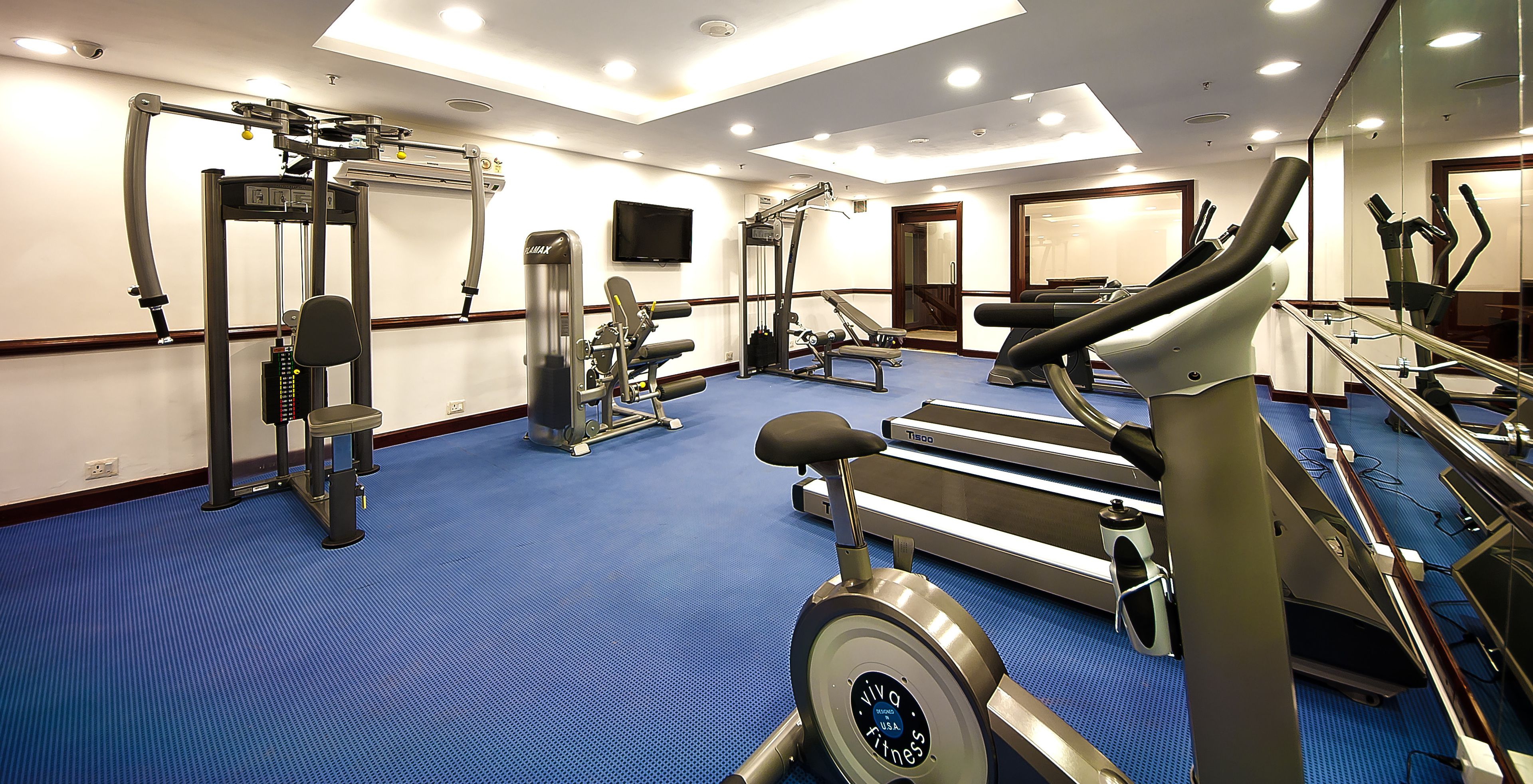 Un gimnasio con equipo de ejercicio diverso, alfombra azul y un espejo grande.