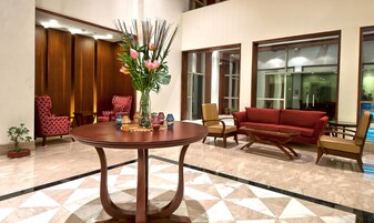 Un hall con una mesa redonda de madera, sillas con estampado rojo, un sofá rojo y un jarrón con flores.