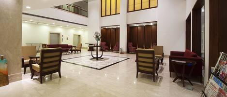 A spacious lobby with multiple seating areas, a central decorative table, and a magazine rack.