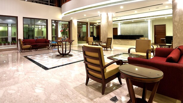 A spacious lobby with a red sofa, beige armchairs, and a glass coffee table.