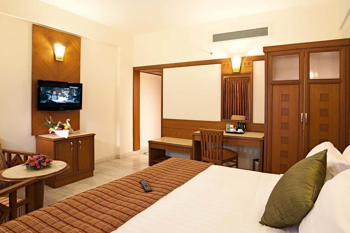 A hotel room with a bed, a desk, a chair, a television, and a wardrobe.