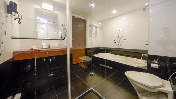 A modern bathroom with a glass shower enclosure, a double sink vanity, and a toilet. - JP Hotel (Chennai)