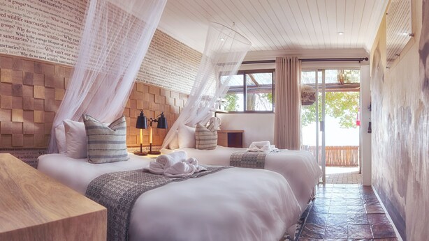 A hotel room with two beds, a wooden headboard, a canopy, and a view of the outdoors.