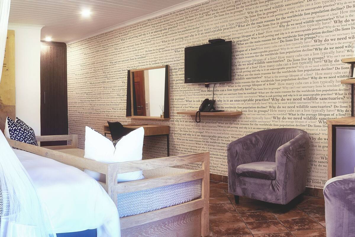 Une chambre d’hôtel comprenant un lit, une table de chevet, une chaise, un téléviseur et un mur orné d’un texte imprimé.