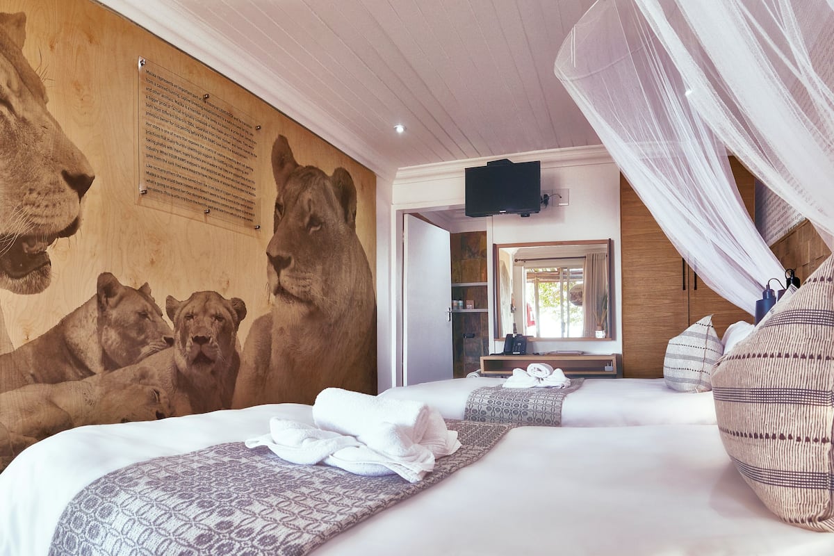 Une chambre d’hôtel avec une grande fresque représentant un lion sur le mur, un lit recouvert d’une courtepointe à motifs et un lit à baldaquin.