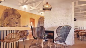 A restaurant with a large lion mural, wicker chairs, a round table, and a stone wall.