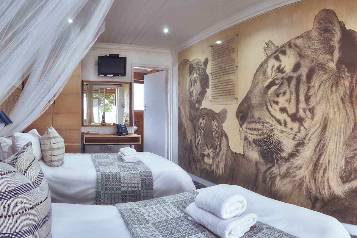 Une chambre d’hôtel avec deux lits, une grande fresque représentant un tigre, une télévision et un panneau indiquant « Contribuez au progrès ».