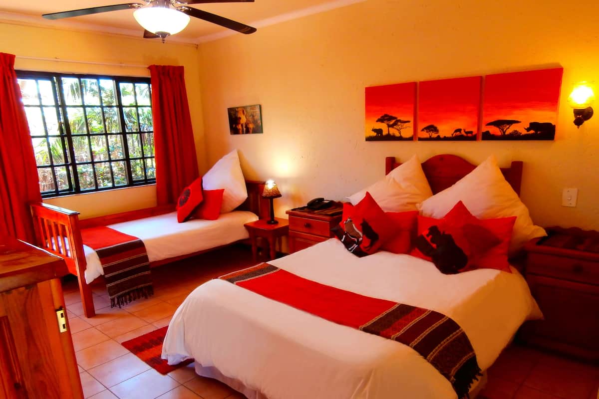 A hotel room with two beds, a desk, a nightstand, a lamp, and a window with curtains.