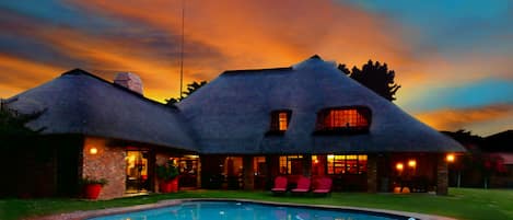Uma casa com piscina, telhado de palha e um espaço de pátio bem iluminado.