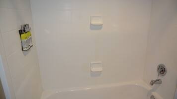 A white-tiled bathroom with a bathtub, two soap dispensers, and a set of toiletries on the left.
