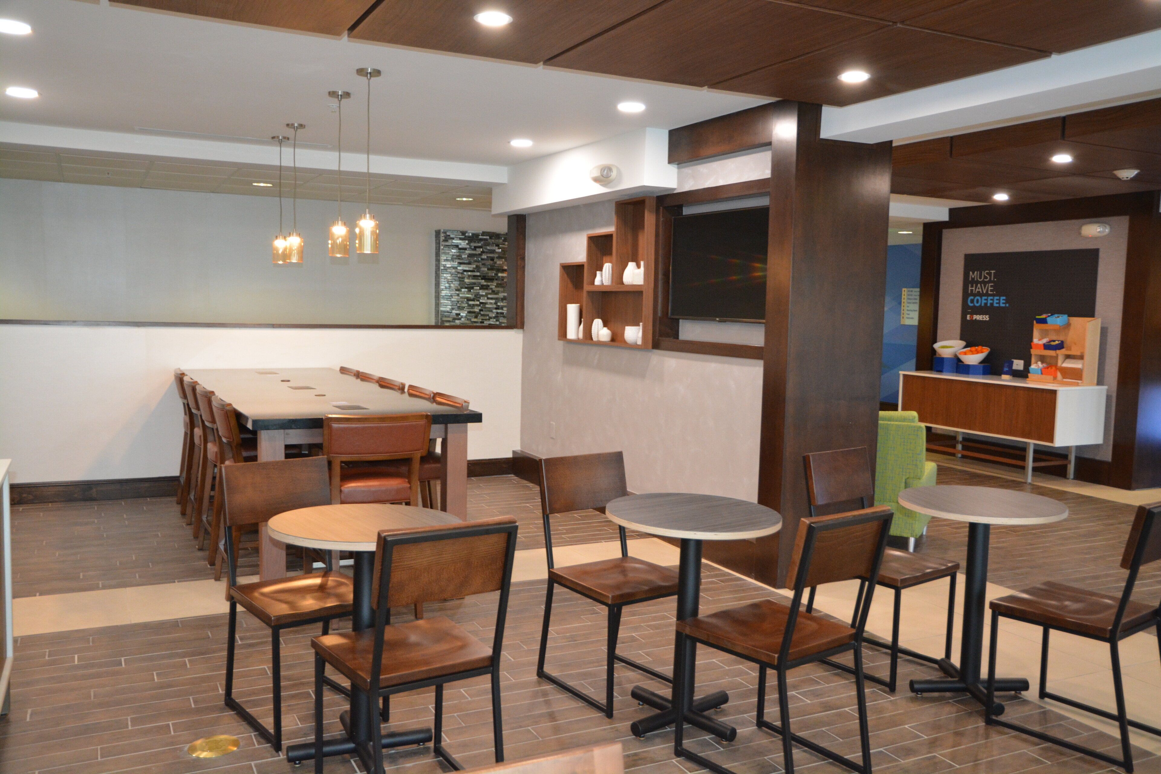Un interior de cafetería moderna con diversas opciones de asientos, incluyendo mesas y sillas, un expositor de cafeteras y luminarias colgantes.
