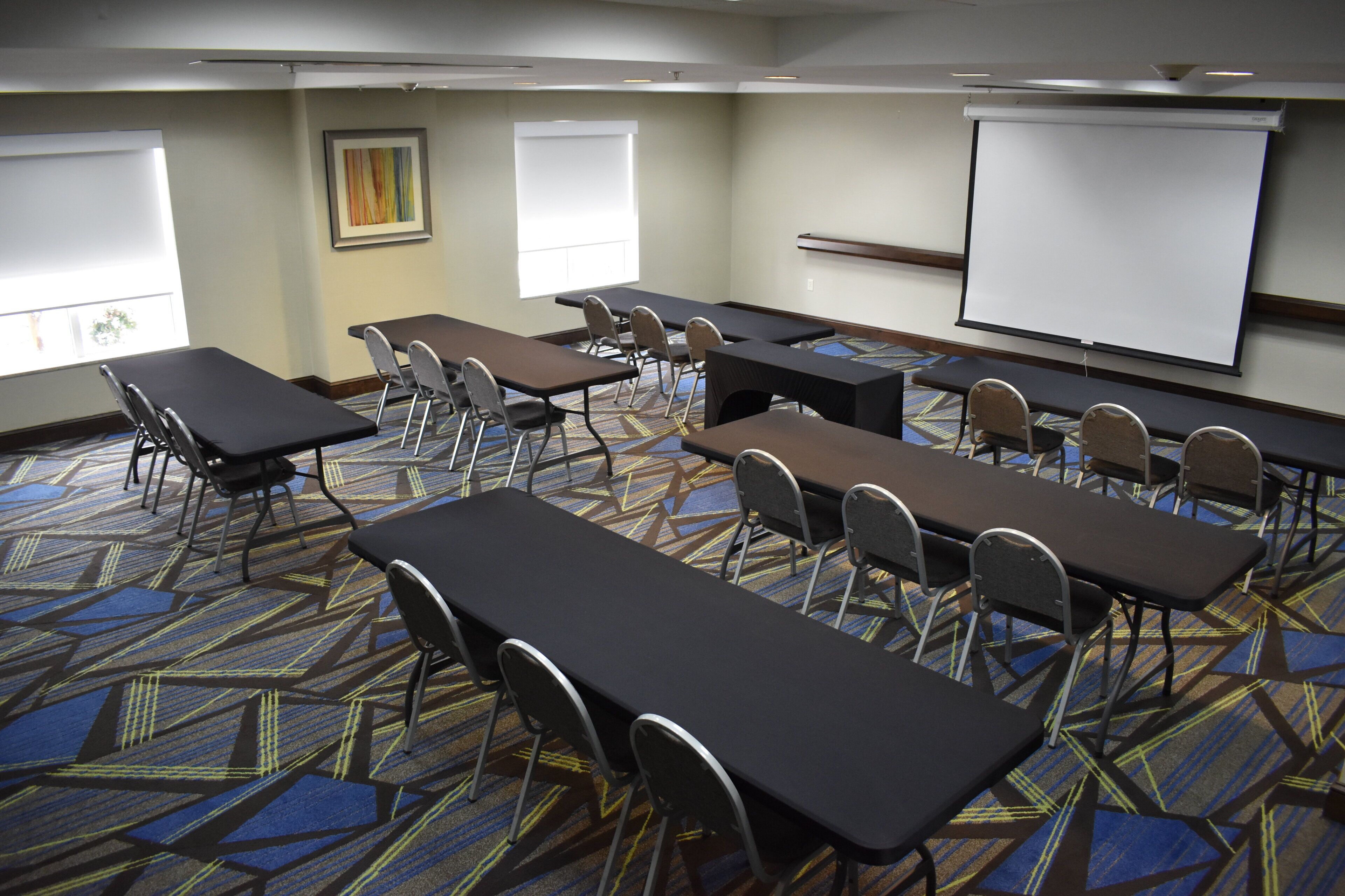 A conference room with tables and chairs, a projector screen, and a large window.