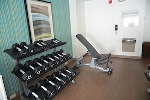 Gimnasio con mancuernas, banco y un cartel en la pared.
