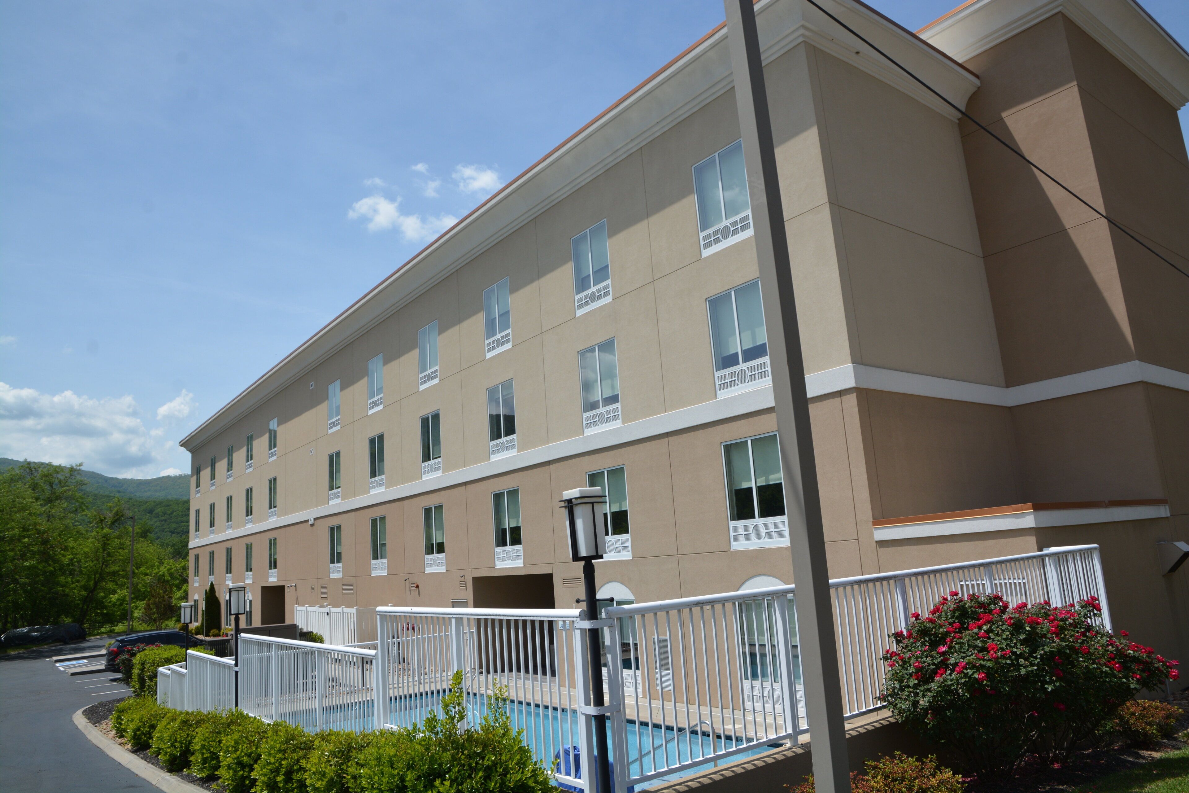 A multi-story hotel with a swimming pool, surrounded by greenery and a parking area.