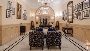 Una sala elegante con una larga mesa, dos sillones azules, una araña y cuadros enmarcados en las paredes.