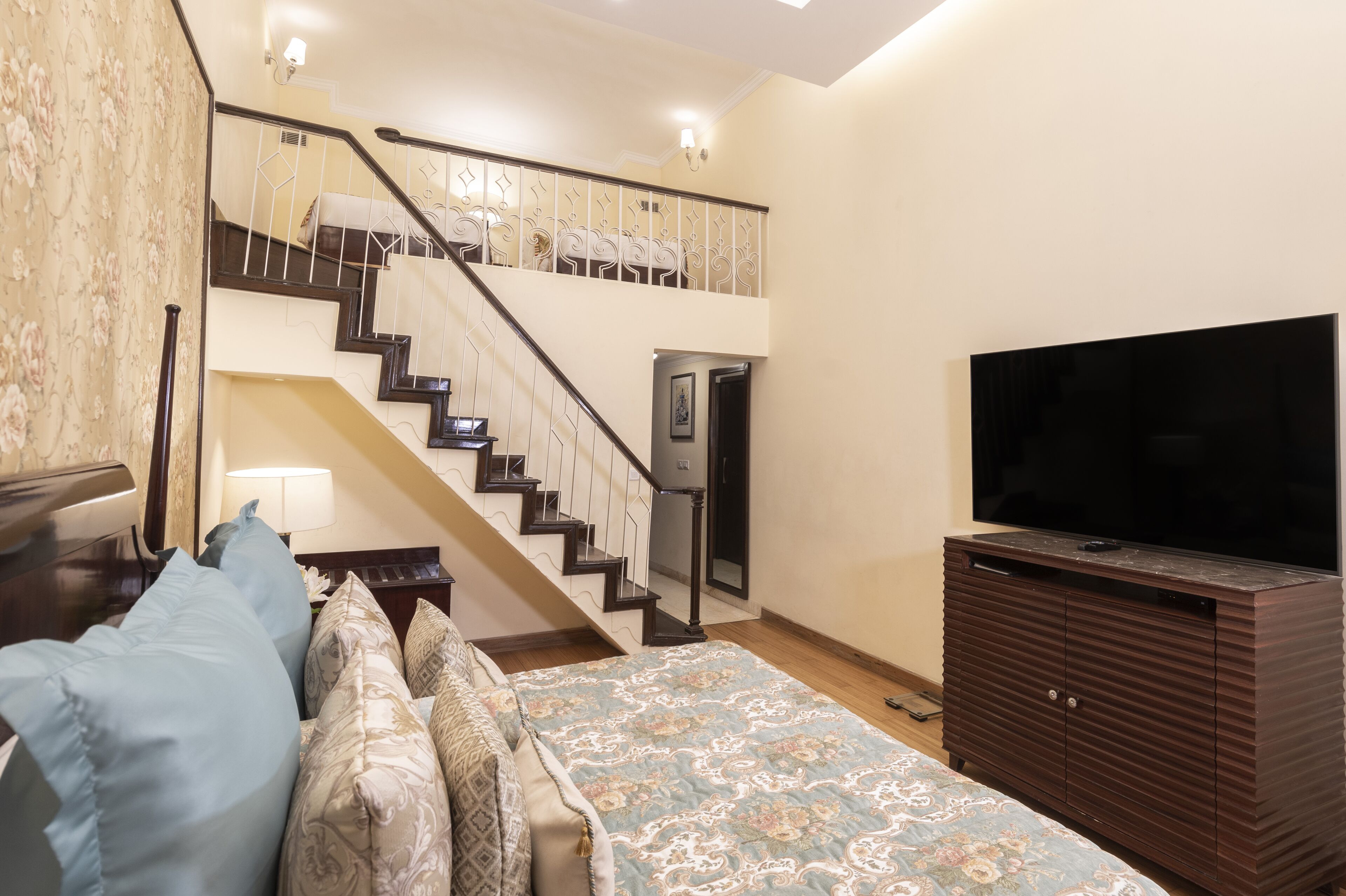 A bedroom with a bed, a TV, a dresser, a staircase, and a door.