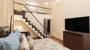 A bedroom with a bed, a TV, a dresser, a staircase, and a door.