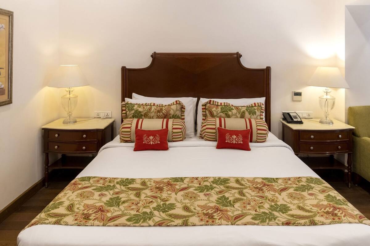 Habitación de hotel con una cama grande, dos mesitas de noche, una silla y una lámpara a cada lado.